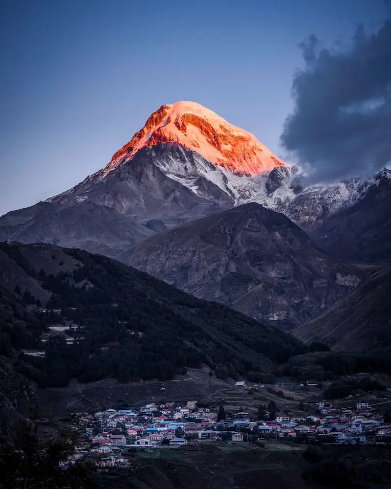 Mount Kazbek lit at sunset above a valley town